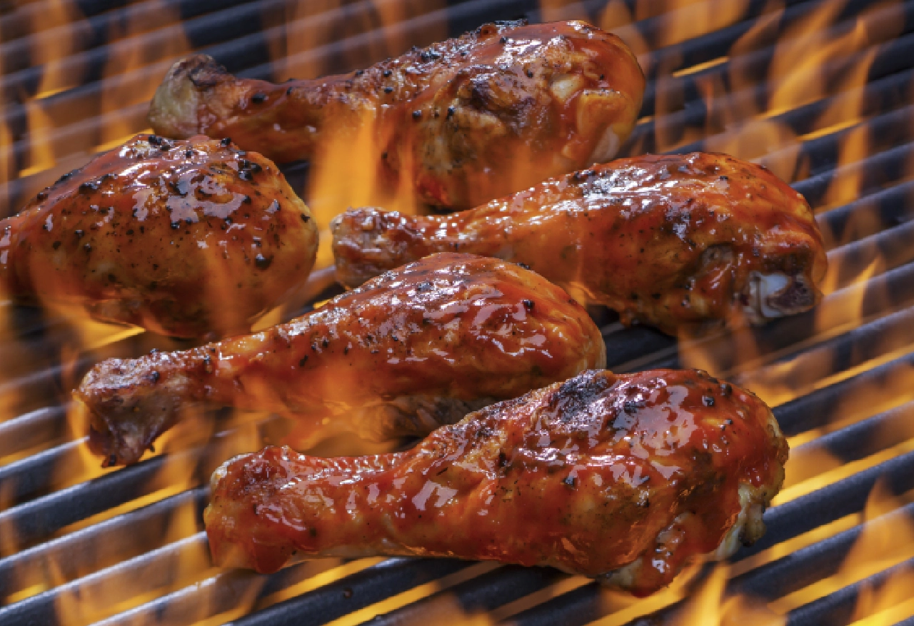 Grilled barbecue chicken drumsticks on flame.