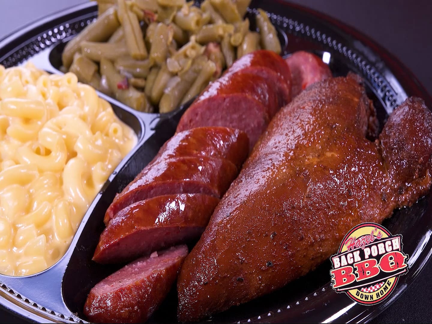 A black bowl of food with meat, macaroni and cheese and green beans.